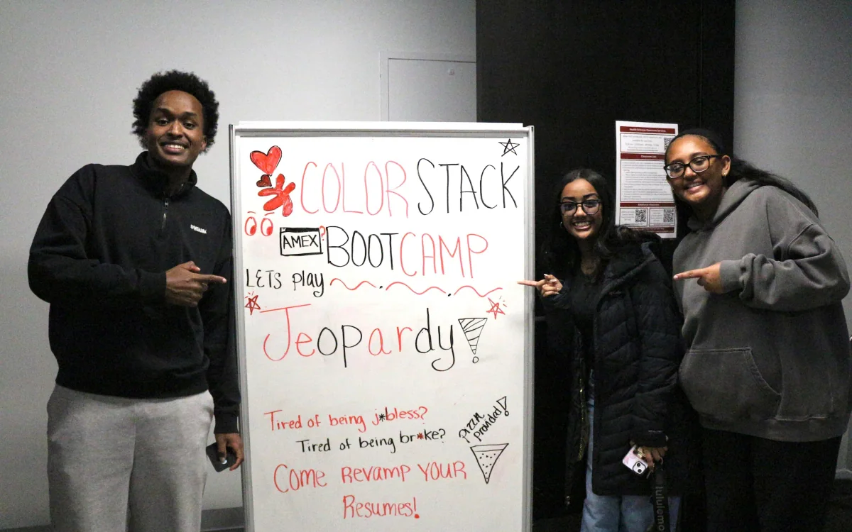 Three ColorStack UMN members standing beside a whiteboard reading "ColorStack Bootcamp, let's play Jeopardy" with résumé and interview categories
