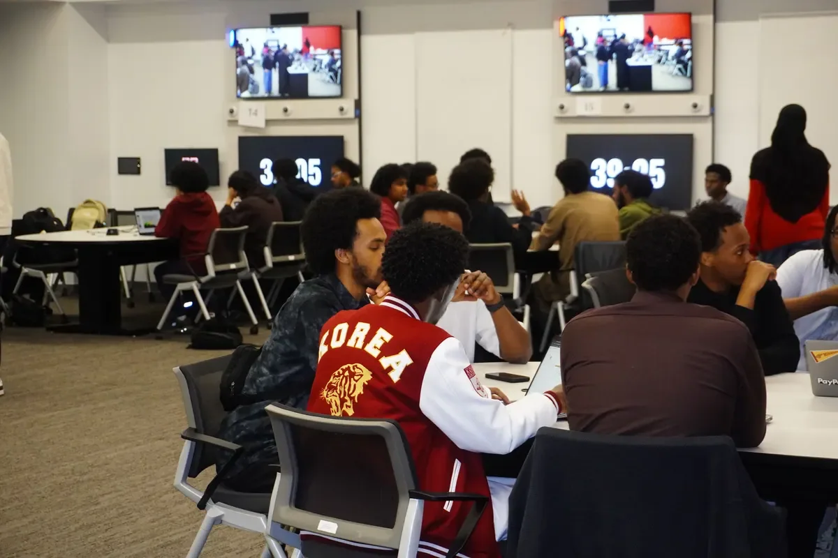 Students at round tables with laptops during the Ideathon, a countdown timer on the screen at the front of the room