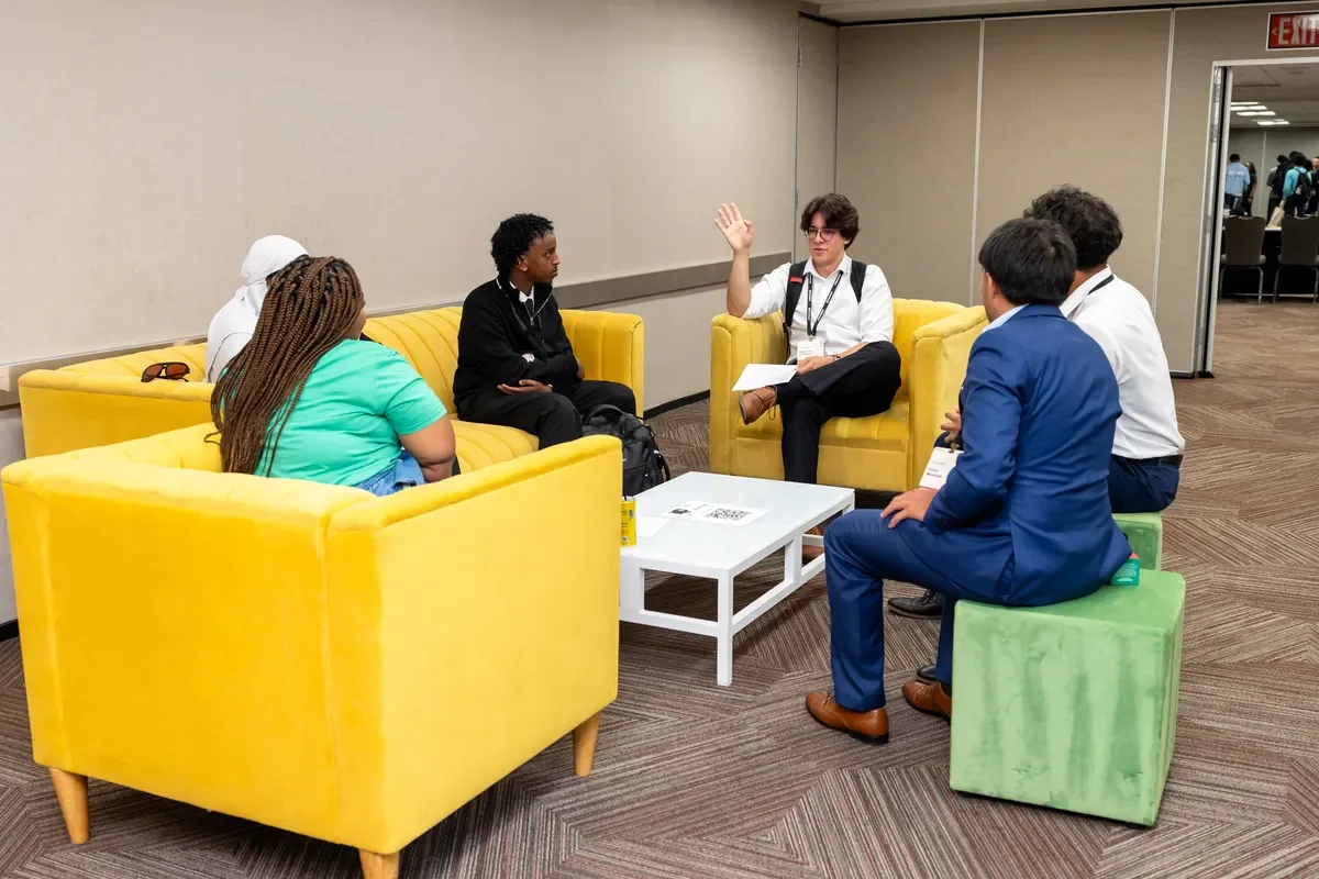 Five people talking in a conference lounge seating area, one gesturing with a raised hand
